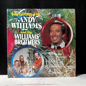 Może przedstawiać: Vintage okładka albumu winylowego "Christmas with Andy Williams and the Williams Brothers". Okładka przedstawia portret Andy'ego Williamsa w czerwonej bombce, z braćmi Williams w drugiej bombce. Tytuł albumu jest w kolorze żółtym i białym.