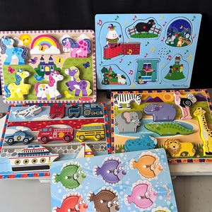 May include: A collection of five wooden peg puzzles featuring colorful illustrations of ponies, nursery rhymes, vehicles, wild animals, and fish. Each puzzle board contains various shaped wooden pieces with small knobs for easy handling and placement.