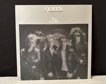 May include: A black and white photo of the band Queen on the cover of their album "The Game". The band members are wearing leather jackets and are looking at the camera.