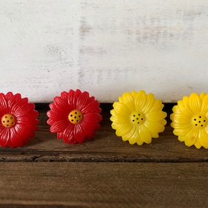 Puede incluir: Cuatro saleros y pimenteros de plástico con forma de flor. Dos son rojos y dos son amarillos.