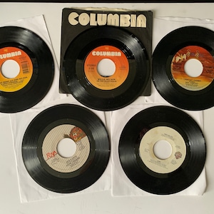 May include: Five black vinyl records with white labels. The labels feature the Columbia Records logo and song titles. The records are on white paper squares.