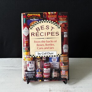 May include: A cookbook titled "Best Recipes" with a red, white, and black cover. The cover features a variety of food products, including boxes, bottles, cans, and jars. The book is by Ceil Dyer.
