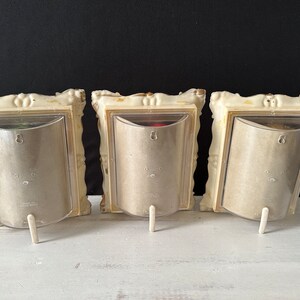 May include: Three ornate white picture frames with gold accents and clear plastic inserts. Each frame has a small white stand.