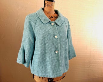 May include: A light blue jacket with three white buttons and a rounded collar. The jacket has three-quarter length sleeves with a flared design. The fabric has a textured appearance. The jacket is displayed on a mannequin.