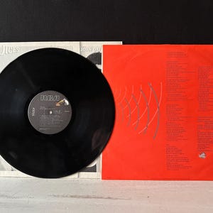 May include: A black vinyl record with a red and white RCA Victor label. The record is titled "Voices" by John Oates. The back cover of the record is red with white text and a silver graphic.