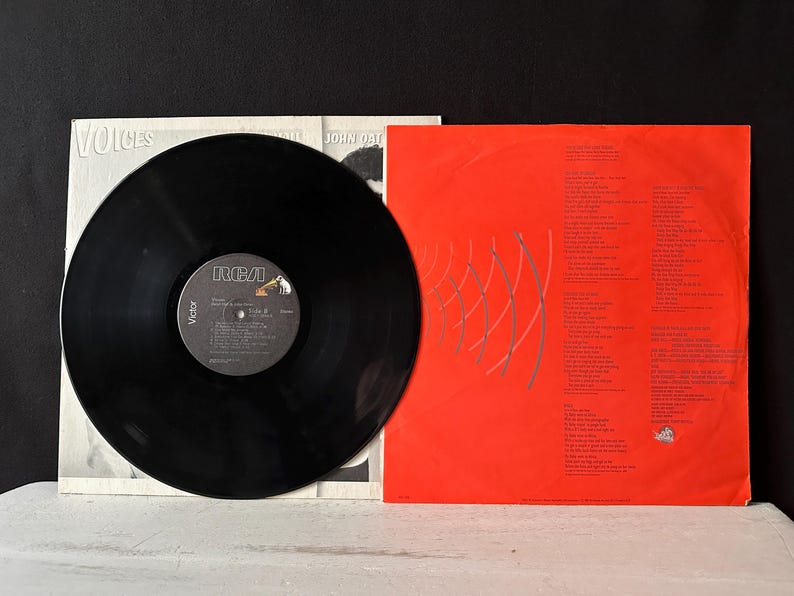 May include: A black vinyl record with a red and white RCA Victor label. The record is titled "Voices" by John Oates. The back cover of the record is red with white text and a silver graphic.