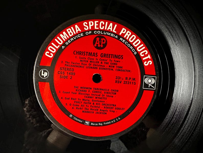 May include: Red and white vinyl record label with the text "Columbia Special Products" and "Christmas Greetings". The label lists the songs "Santa Claus Is Comin' To Town", "The Twelve Days Of Christmas", "Count Your Blessings", "God Rest Ye Merry, Gentlemen", "O Come All Ye Faithful", and "Hark! The Herald Angels Sing".