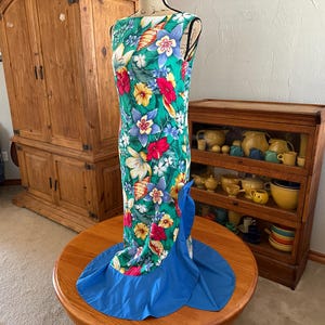 May include: A green and blue floral print dress with a blue ruffle at the bottom. The dress has a sleeveless bodice and a fitted silhouette.