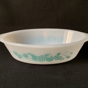 May include: White oval baking dish with a green and white fruit design. The design features a pineapple, pear, apple, grapes, and cherries.