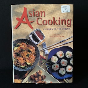 Könnte beinhalten: Ein Kochbuch mit dem Titel "Asian Cooking: Cuisines of the Orient" mit einem stilisierten roten und weißen "A" auf dem Cover. Das Cover zeigt Fotos von asiatischen Speisen, darunter Sushi, Nudeln und Spieße.