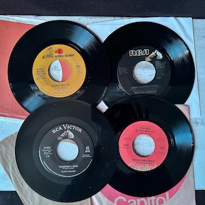 Könnte beinhalten: Vier Vintage-Schallplatten werden gezeigt, jede mit einer schwarzen Oberfläche und einem farbenfrohen Etikett. Die Etiketten enthalten Text und Logos, darunter "Reprise Records", "RCA Victor" und "Capitol". Die Schallplatten befinden sich in ihren Originalhüllen.
