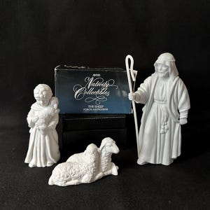 Puede incluir: Un juego de nacimiento de porcelana blanca con un pastor con un bastón, una figura joven sosteniendo un cordero y una oveja reclinada. El juego incluye una caja que dice "Avon Nativity Collectibles".