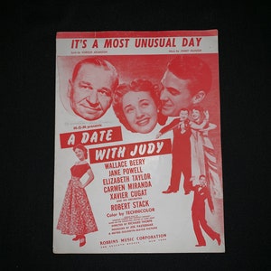 May include: A red and white sheet music cover for the song "It's a Most Unusual Day" from the film "A Date With Judy". The cover features photos of Wallace Beery, Jane Powell, Elizabeth Taylor, Carmen Miranda, Xavier Cugat, and Robert Stack.