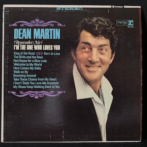 May include: A vintage vinyl record album cover featuring Dean Martin. The cover is black with a purple border and features a photo of Dean Martin in a white shirt and black jacket. The album title is "I'm the One Who Loves You" and includes the song titles "King of the Road", "The Birds and the Bees", "Red Roses for a Blue Lady", "Welcome to My World", "Here Comes My Baby", "Walk on By", "Bumming Around", "Take These Chains from My Heart", "I Don't Think You Love Me Anymore", and "My Shoes Keep Walking Back to You".