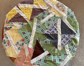 Può includere: Una trapunta circolare con un design patchwork. La trapunta presenta vari tessuti nei toni del giallo, marrone, verde e tessuti fantasia. La trapunta è composta da pezzi triangolari e rettangolari cuciti insieme con strisce bianche.