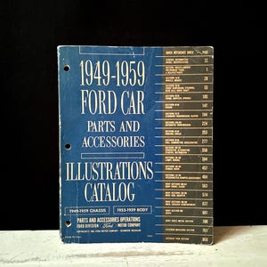 May include: A vintage blue catalogue for 1949-1959 Ford car parts and accessories. The cover features white text, including "Illustrations Catalog" and a list of sections. The catalogue is held together with three rings.
