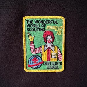May include: A vintage patch with a green background and yellow border. The patch features a cartoon character with red hair and a yellow vest. Text includes "THE WONDERFUL WORLD OF SCOUTING" and "ROUND UP '78". The bottom reads "CHOCCOLOCCO COUNCIL".