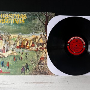May include: A vintage vinyl record with a winter scene on the cover. The cover art features a snowy village with houses and trees. The record is titled "Christmas Greetings" and is a Columbia Special Products release.