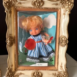 May include: A vintage doll in a blue and white striped dress with a red and white polka dot hat, holding a red plate. The doll is in a plastic frame with a white background and the words "Miss Muffet" printed below.