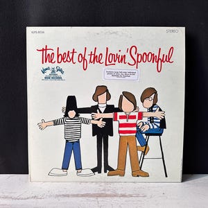 以下が含まれることがあります： 「The Best of the Lovin' Spoonful」のヴィンテージビニールレコードアルバムのカバー。カバーには、バンドメンバーの漫画イラストと、赤いスクリプトで書かれたアルバムタイトルが描かれています。アルバムはステレオ録音です。