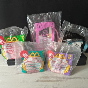 May include: A collection of sealed McDonald's Happy Meal toys in plastic packaging. The toys feature characters from Disney's "The Spirit of Mickey", "Beauty and the Beast", and "Lady and the Tramp", along with a Hello Kitty accessory.