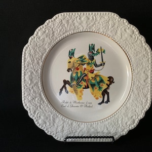 Puede incluir: Plato de cerámica blanco con un borde elevado y adornado. En el centro, una ilustración colorida de un caballero a caballo, con el texto "Ralph de Monthermer d.1325 Earl of Gloucester & Stafford".