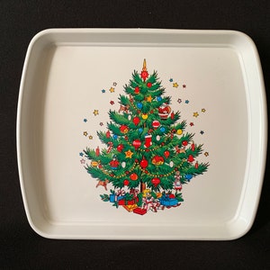 Può includere: Vassoio da portata in plastica bianca con un design a forma di albero di Natale. L'albero è decorato con ornamenti, luci e bastoncini di zucchero. Ci sono anche piccole figure di bambini e animali intorno alla base dell'albero.
