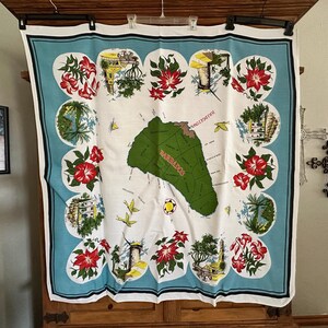 May include: A vintage white and blue Barbados souvenir textile. The center features a green map of Barbados with the word "Barbados" in red. The border has red flowers, buildings, and the word "Bridgetown".