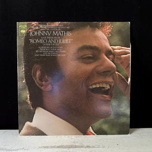 May include: Vintage vinyl record album cover featuring Johnny Mathis. The album is titled "Romeo and Juliet" and includes the song "A Time for Us." The cover displays a smiling portrait of Johnny Mathis. The album is from Columbia Records.