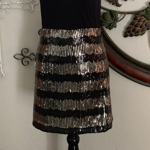 May include: A black and gold sequined mini skirt with a horizontal stripe pattern.