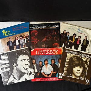 May include: A collection of vintage vinyl records featuring album covers from artists like REO Speedwagon, Tom Jones, Loverboy, and Donny Osmond. The covers display band photos and song titles, with a variety of colors and designs.