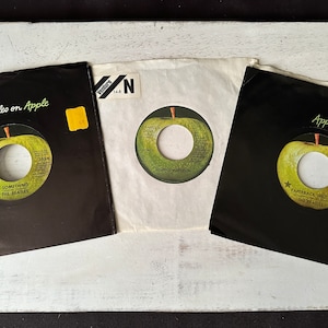 May include: Three black vinyl records with green apple labels. The Beatles "Something" and "Paperback Writer", and George Harrison "Bangla Desh".