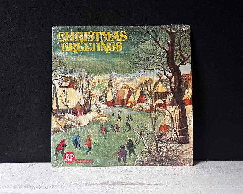 May include: A vintage Christmas record album cover with a snowy winter scene. The cover features a small village with houses, trees, and people walking in the snow. The text "Christmas Greetings" is printed in yellow on a green background.