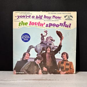 以下が含まれることがあります： The Lovin' Spoonfulの「You're a Big Boy Now」のヴィンテージビニールレコードアルバムカバー。カバーには、バンドの写真と像、そして「Darling, Be Home Soon」というテキストが掲載されています。