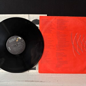 May include: A black vinyl record with a red and white label that says "RCA Victor" and "Voices" by John Oates. The record is on a white background with a red and white album cover that says "Voices" by John Oates.