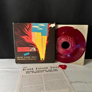 Könnte beinhalten: Vintage RCA Victor Schallplattenalbum und Vinyl-Schallplatte. Das Albumcover zeigt eine farbenfrohe Illustration des Grand Canyon. Die rote Vinyl-Schallplatte ist neben dem Album zu sehen. Ein bedrucktes Blatt mit Text ist ebenfalls vorhanden.