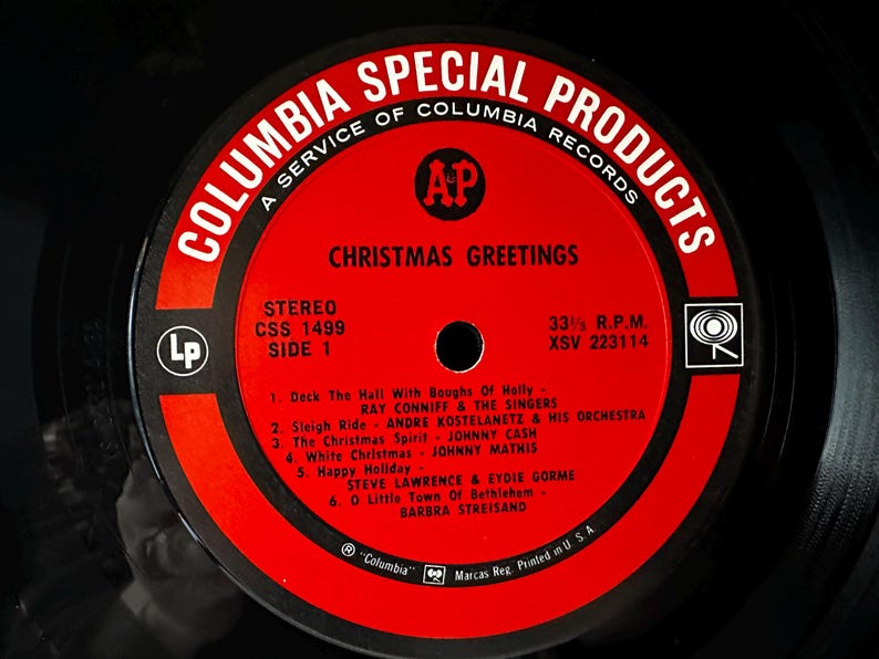 May include: Red and white vinyl record label with the text "Columbia Special Products" and "Christmas Greetings". The label lists six Christmas songs with the artists and a stereo record number.