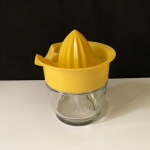 Puede incluir: Un exprimidor de cítricos de plástico amarillo con base de vidrio. El exprimidor tiene un cono estriado para exprimir cítricos.