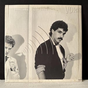 May include: A black and white photo of two men, Daryl Hall and John Oates, on a record album cover. The album cover is titled "Voices".