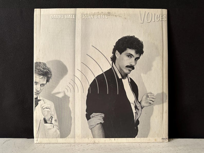 May include: A black and white photo of two men, Daryl Hall and John Oates, on a record album cover. The album cover is titled "Voices".