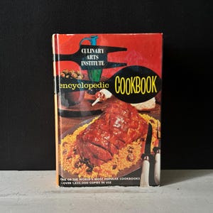 May include: A vintage cookbook with a red cover featuring the text "Culinary Arts Institute Encyclopedic Cookbook." The cover displays a picture of a cooked meat dish on a bed of yellow rice. The book's title is in a black oval.