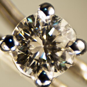 Puede incluir: Primer plano de un diamante redondo y transparente con engaste de plata. El diamante est&aacute; engastado en un anillo con cuatro garras.