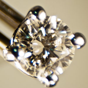 Puede incluir: Primer plano de un diamante redondo y transparente engastado en un engaste de garras de plata. El diamante refleja la luz, creando un efecto brillante.