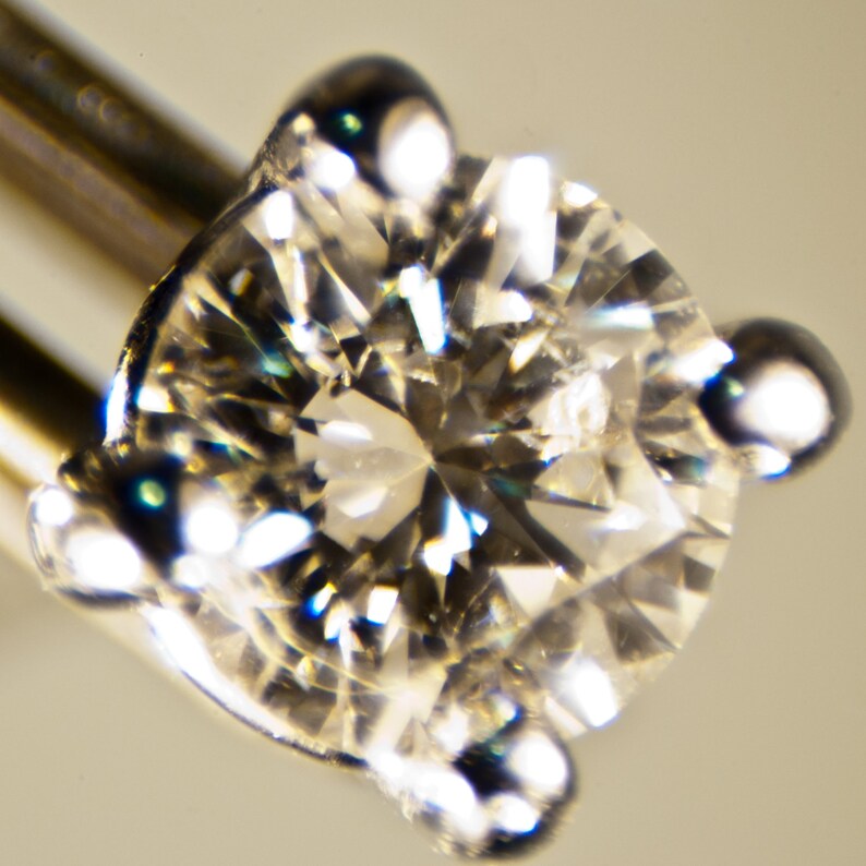 Puede incluir: Primer plano de un diamante redondo y transparente engastado en un engaste de garras de plata. El diamante refleja la luz, creando un efecto brillante.