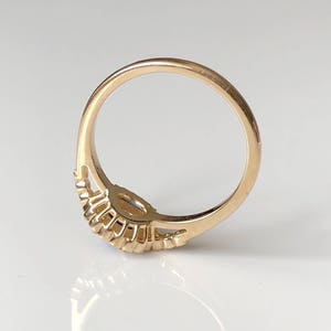 K&ouml;nnte beinhalten: Ein goldener Ring mit einem einzigen, runden, klaren Edelstein, der in der Mitte sitzt. Die Ringschiene ist mit einer Reihe kleiner, runder Edelsteine auf jeder Seite des Mittelst&uuml;cks verziert.