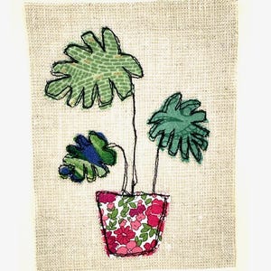 May include: A green potted plant with three leaves in a pink and white floral pot. The plant is on a beige background.