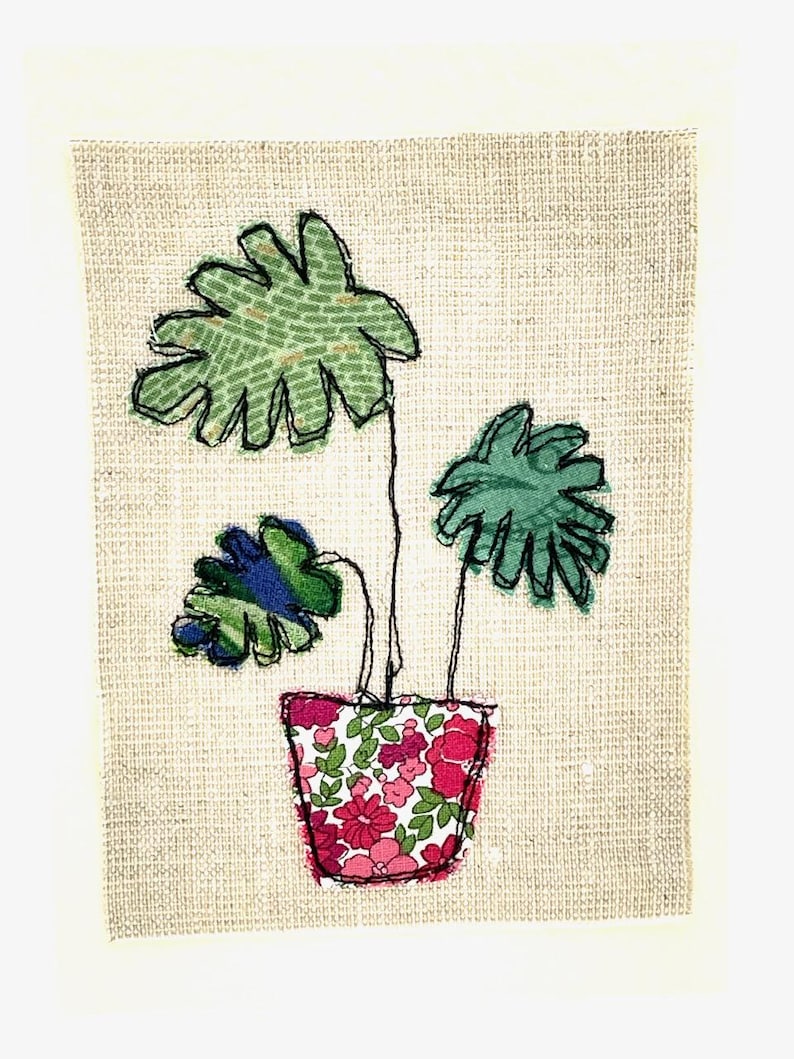 May include: A green potted plant with three leaves in a pink and white floral pot. The plant is on a beige background.