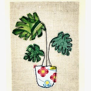 May include: A green plant with large leaves in a white pot with pink and yellow flowers. The pot is on a beige background.