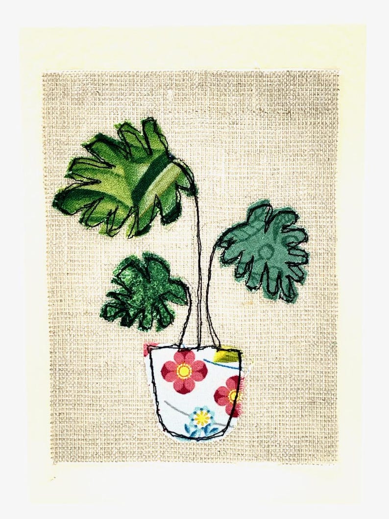 May include: A green plant with large leaves in a white pot with pink and yellow flowers. The pot is on a beige background.