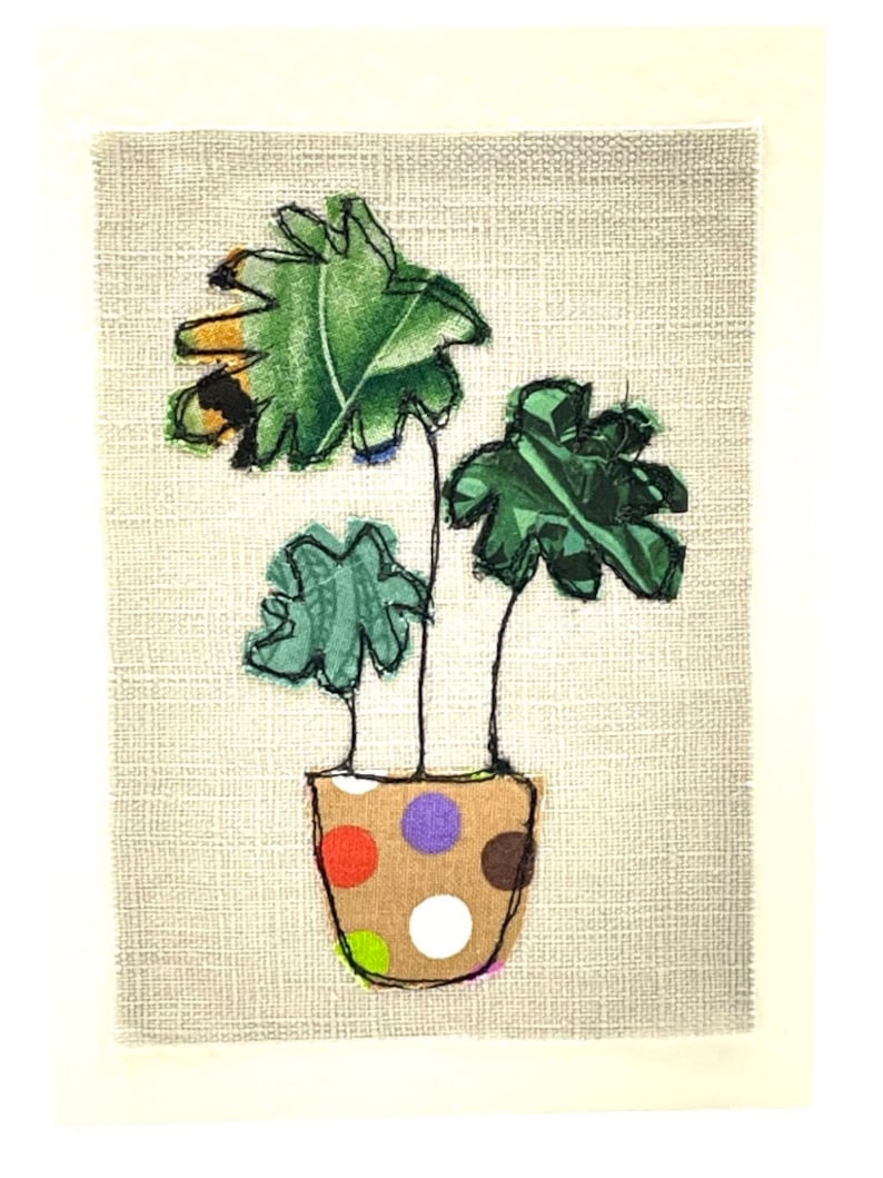 May include: A potted plant with three green leaves in a brown pot with white polka dots. The pot has red, orange, purple, and brown polka dots.